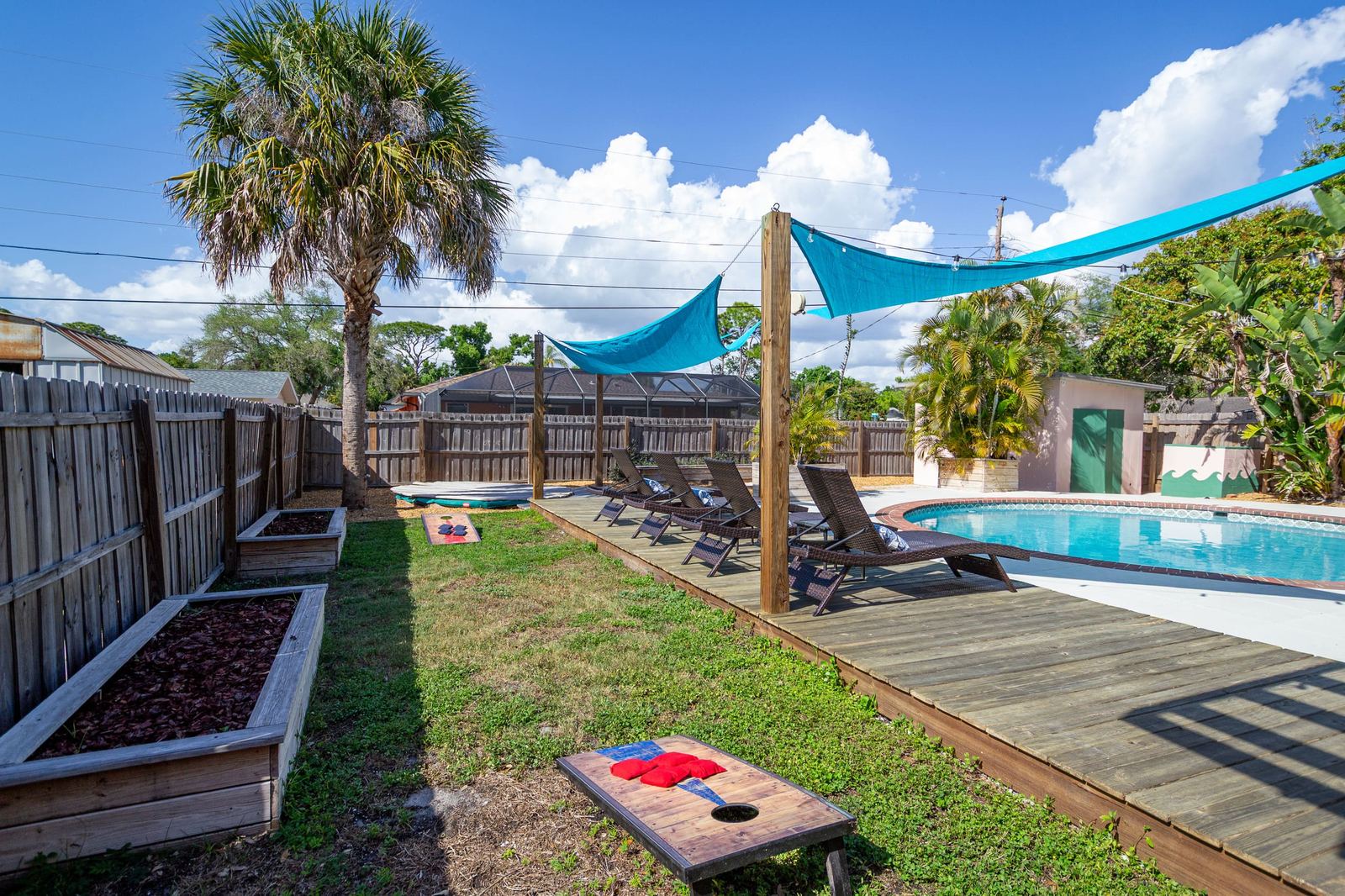 Fenced backyard with cornhole boards and garden beds
